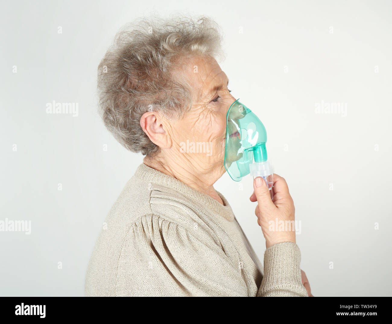 Elderly woman using asthma machine on light background Stock Photo