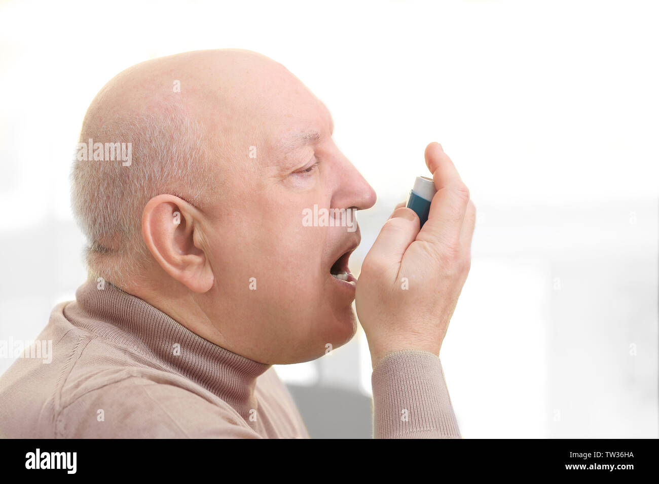 Senior man using asthma inhaler on light background Stock Photo