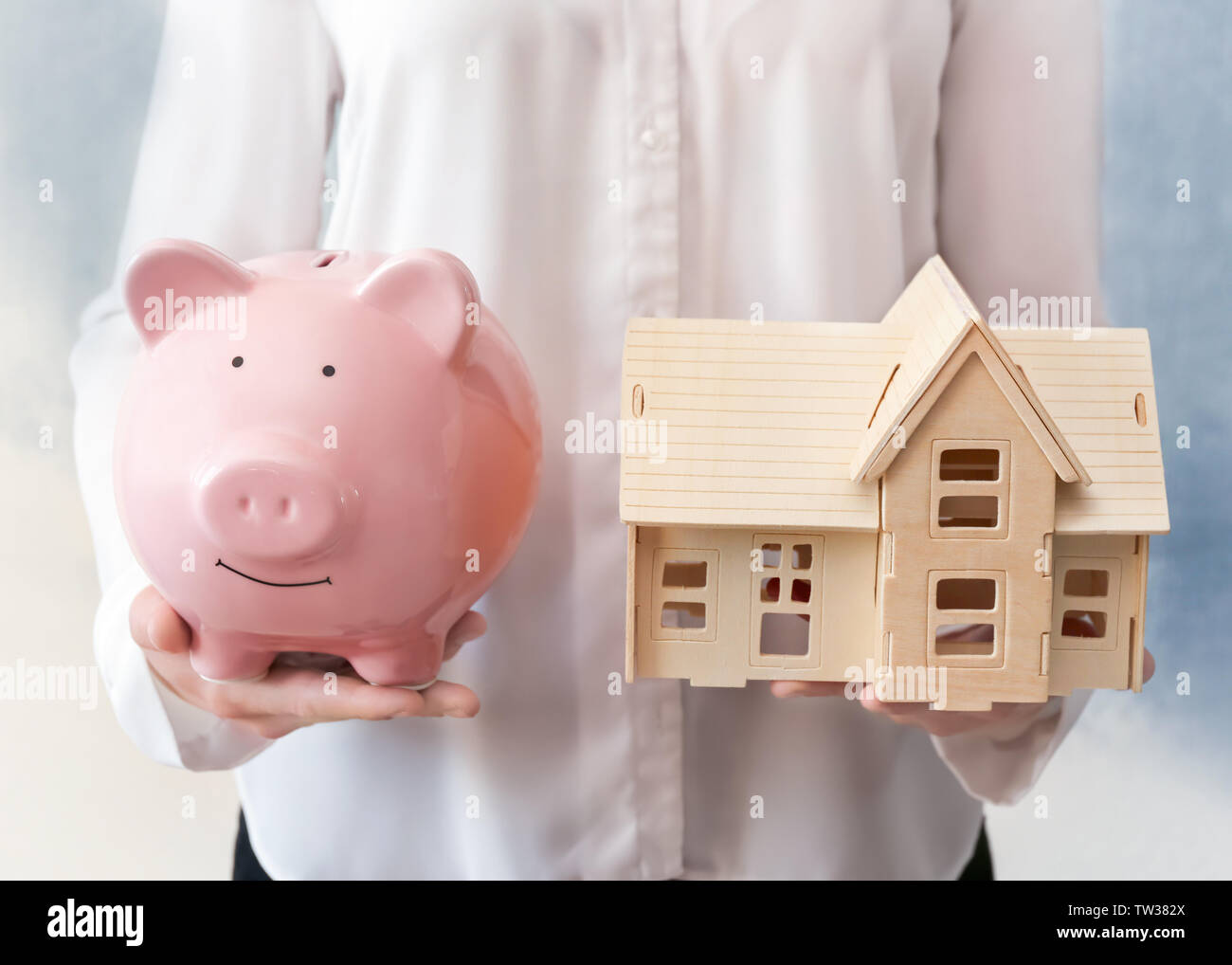 Woman holding piggy bank and model of house in hands. Savings concept ...