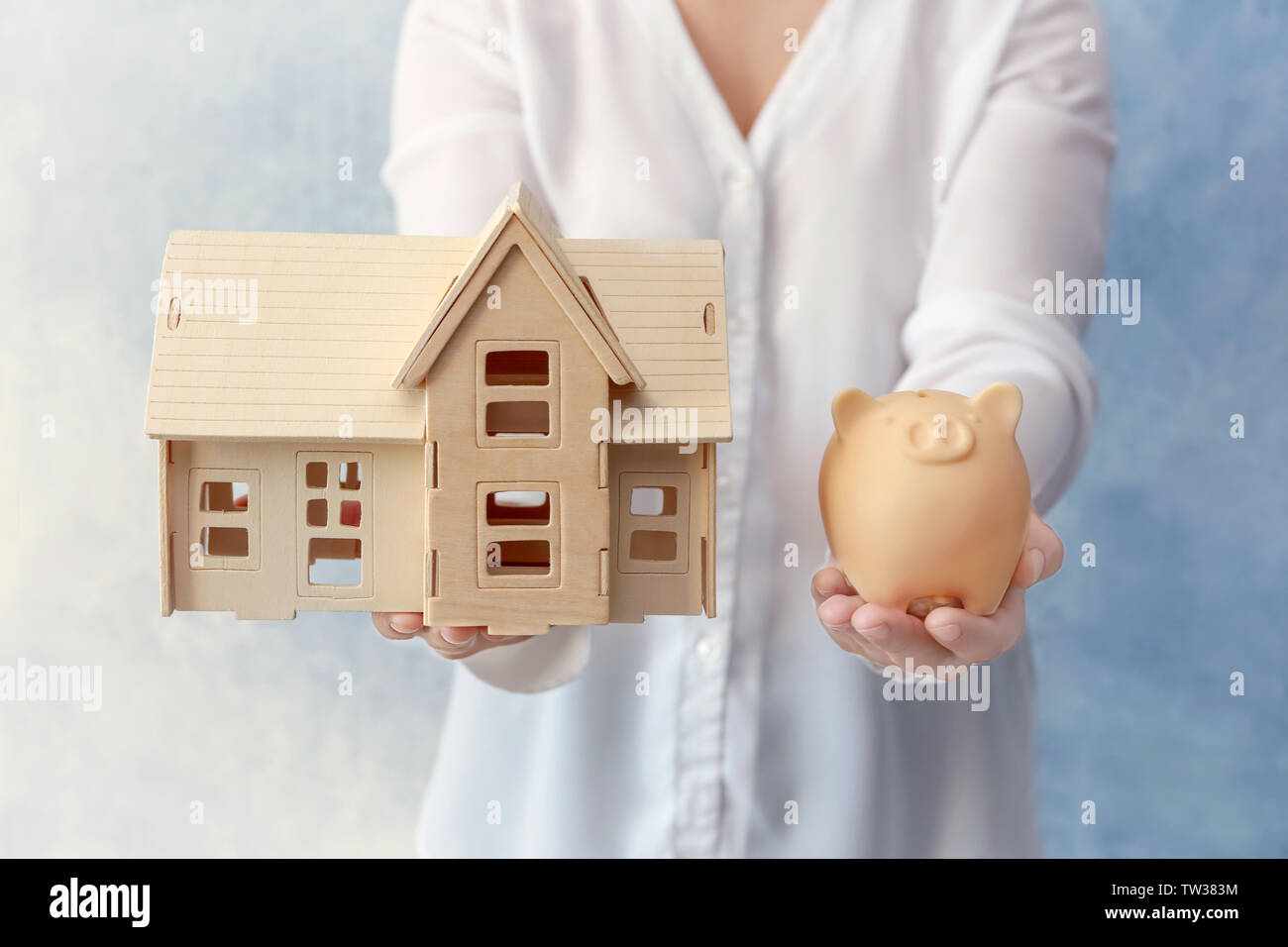 Woman holding piggy bank and model of house in hands. Savings concept ...