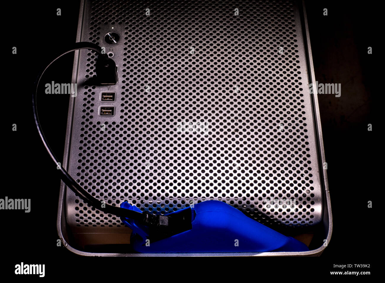 A bright blue external hard drive storage device plugged into a USB port on the front of an Apple Mac Pro desktop computer. Stock Photo