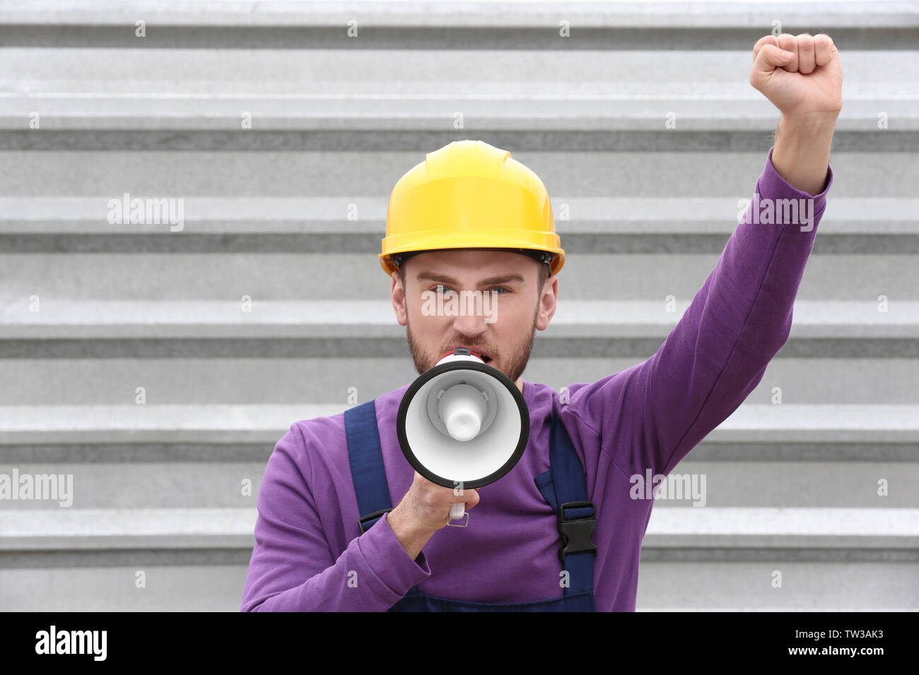 Protesting young man shouting into megaphone against metal fence Stock Photo