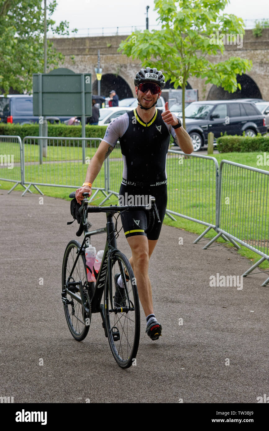 Happy Triathlete gives a thumbs up as he exits the transition area with his bicycle in the rain at the Royal Windsor Triathlon in Berkshire England Stock Photo