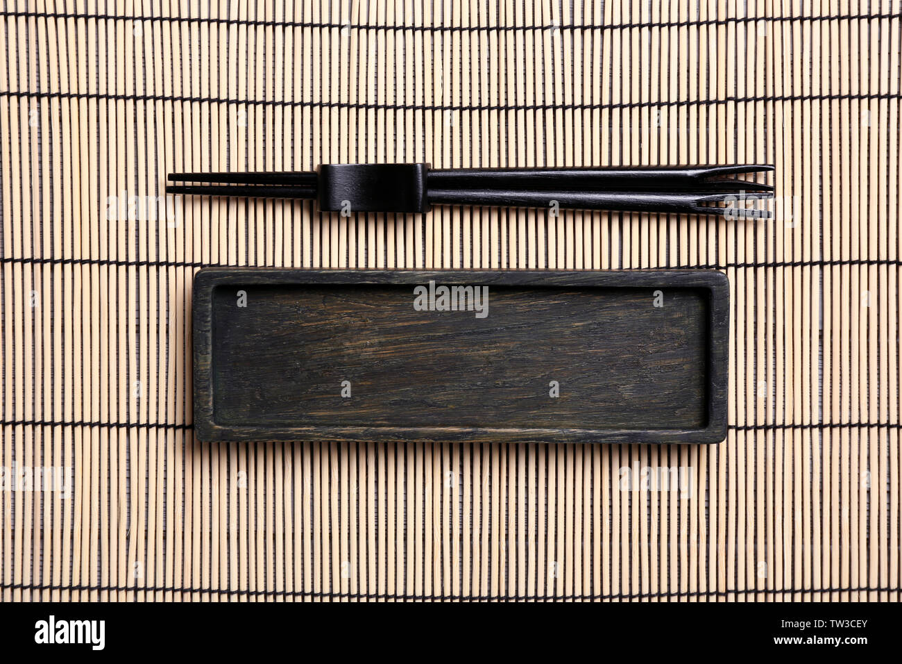 Empty rectangular wooden plate and chopsticks on bamboo mat Stock Photo