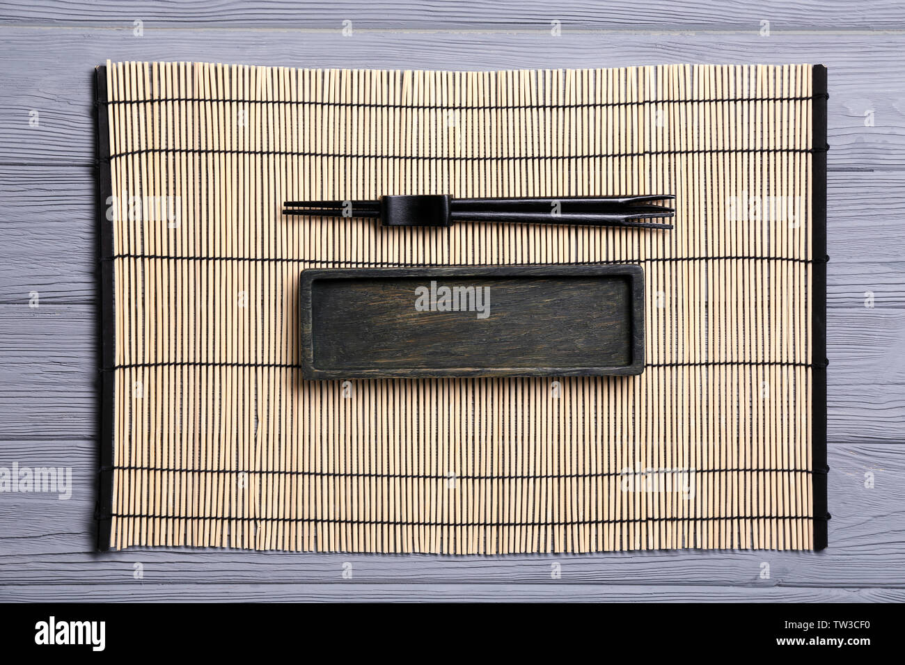 Empty rectangular wooden plate and chopsticks on bamboo mat Stock Photo