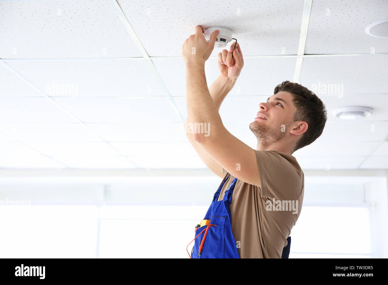 Young electrician installing smoke detector on ceiling Stock Photo