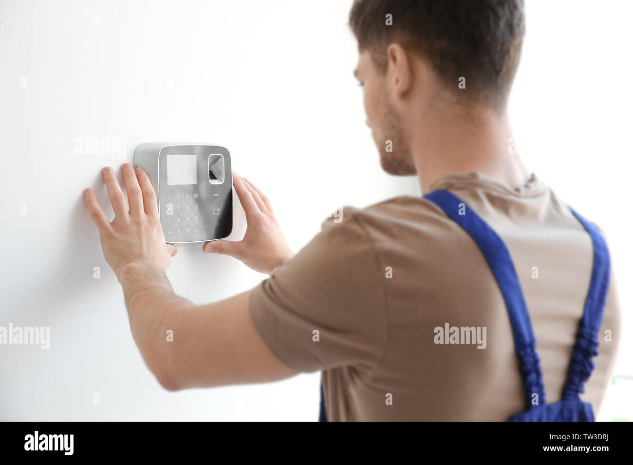 Young electrician installing security alarm on wall Stock Photo