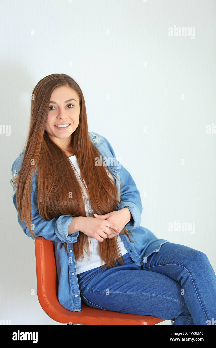 Beautiful woman sitting on chair against light background Stock Photo ...