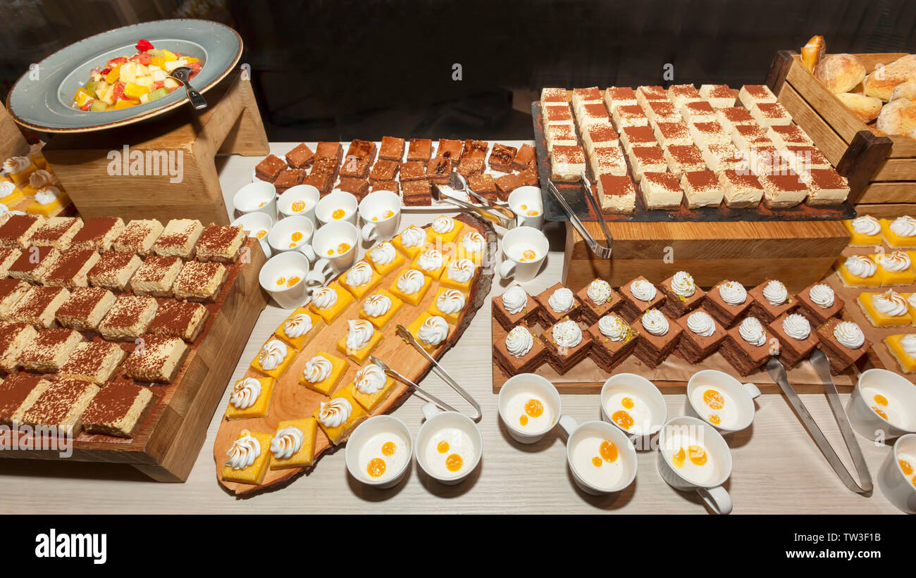 Small assorted cakes lined up decorated on dessert buffet along with fruit salad. Sweet paradise