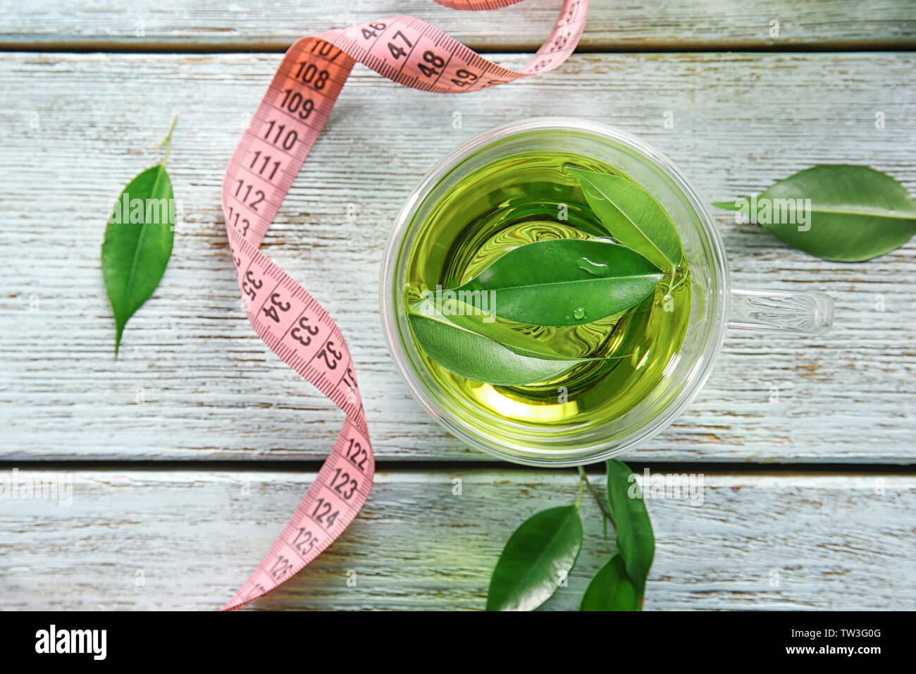Cup of tea with leaves and measuring tape on wooden table. Weight loss ...