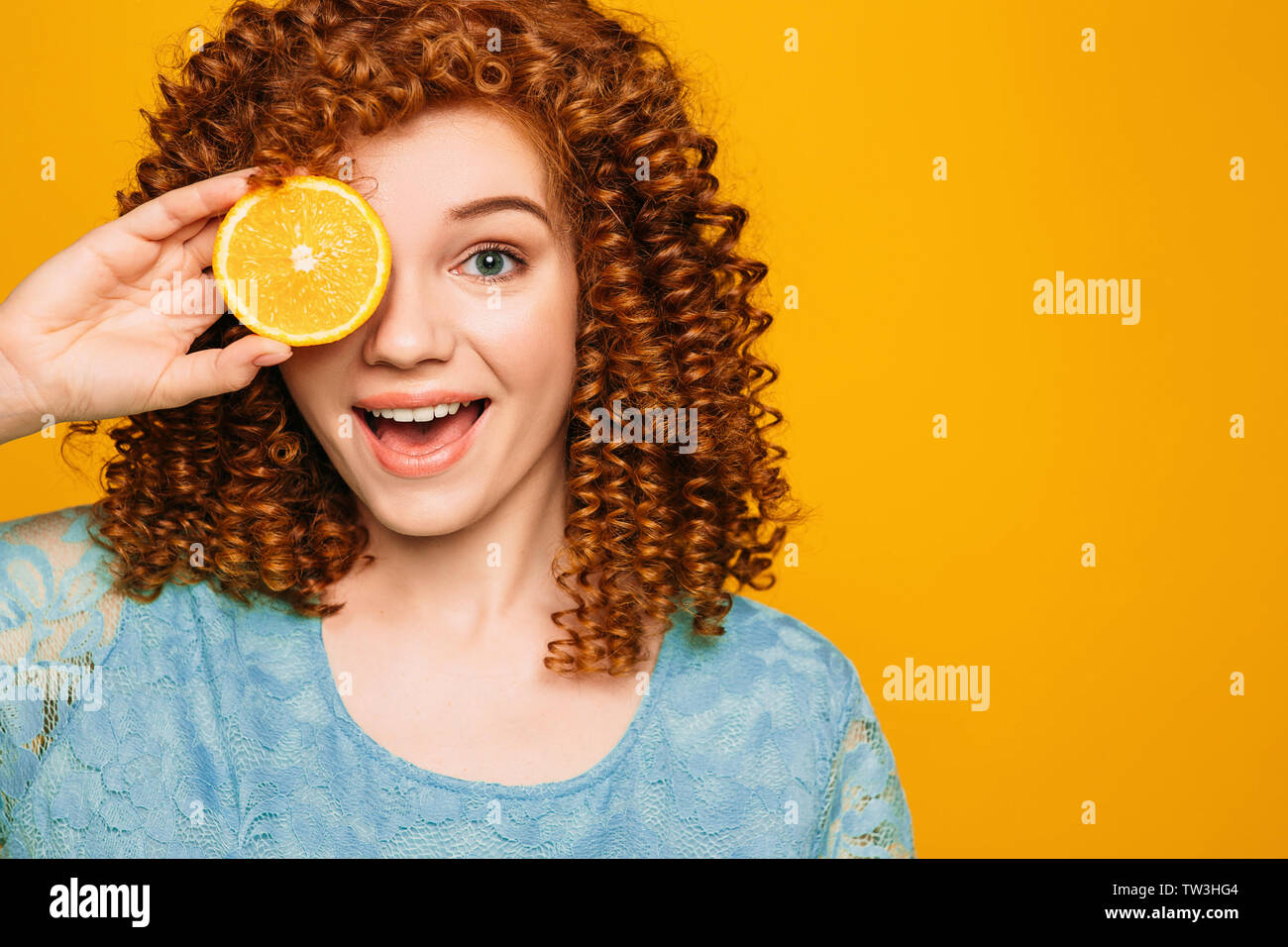 curly red-haired woman with an orange near face with surprise emotion on yellow background. Stock Photo