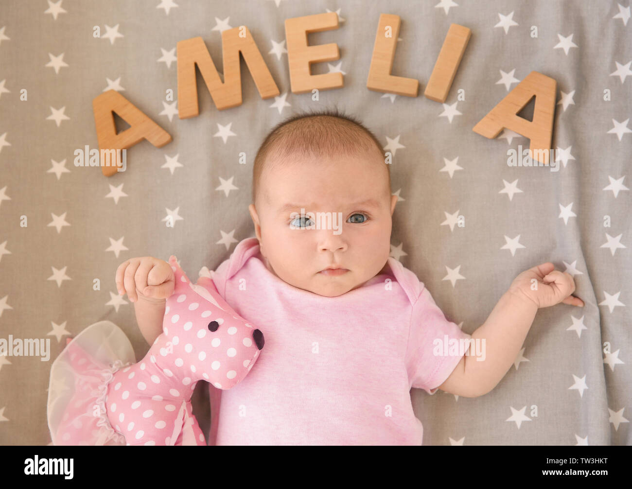 Cute baby lying on bed with toy and word AMELIA composed of wooden