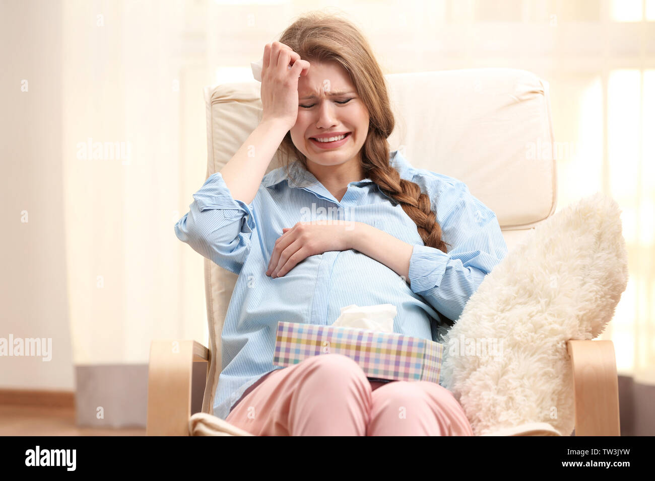 Emotional pregnant woman sitting in arm chair and crying. Pregnancy hormones concept Stock Photo