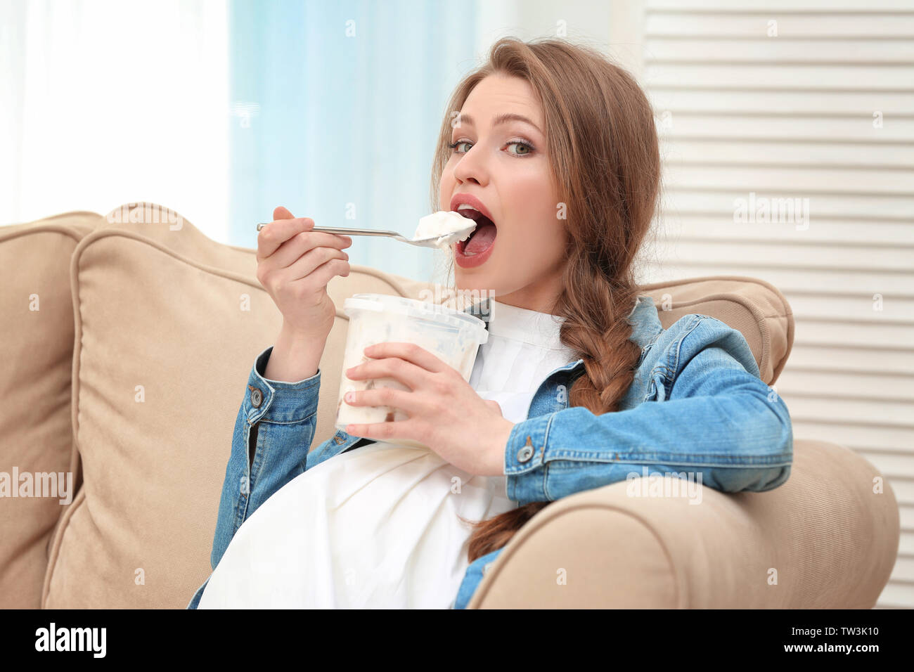 Emotional pregnant woman sitting on sofa and eating icecream