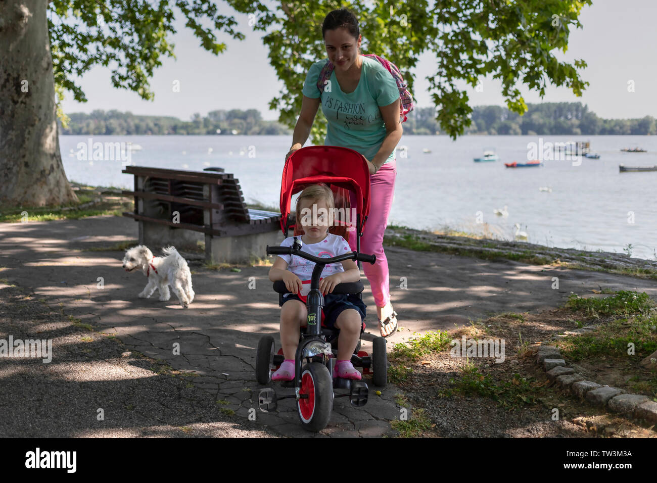 Belgrade, Serbia, June 16th 2019: Mother with little daughter riding tricycle walking along the Danube riverside promenade in Zemun Stock Photo
