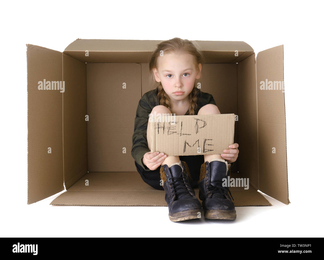 Poor little girl with piece of cardboard sitting in cardboard box on white background Stock Photo
