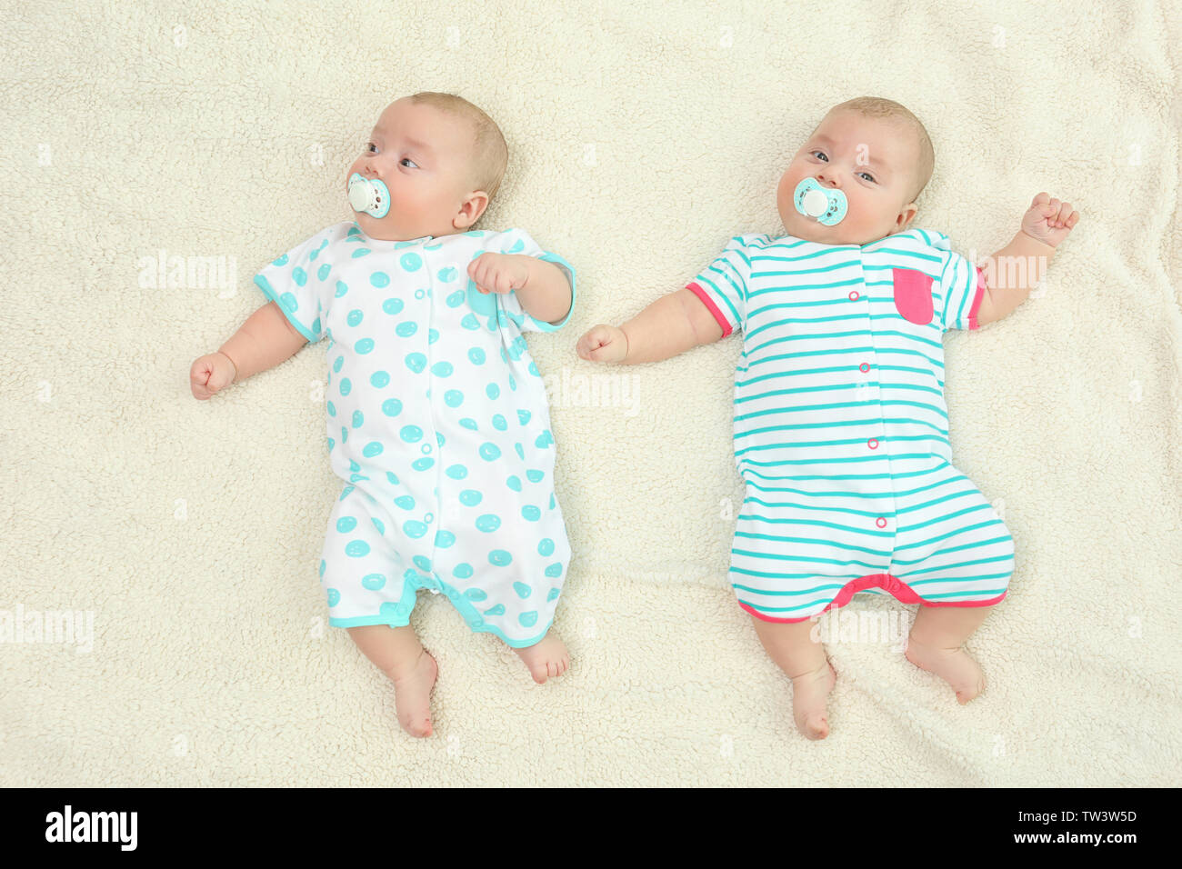 Beautiful baby twins lying with pacifiers on plaid Stock Photo