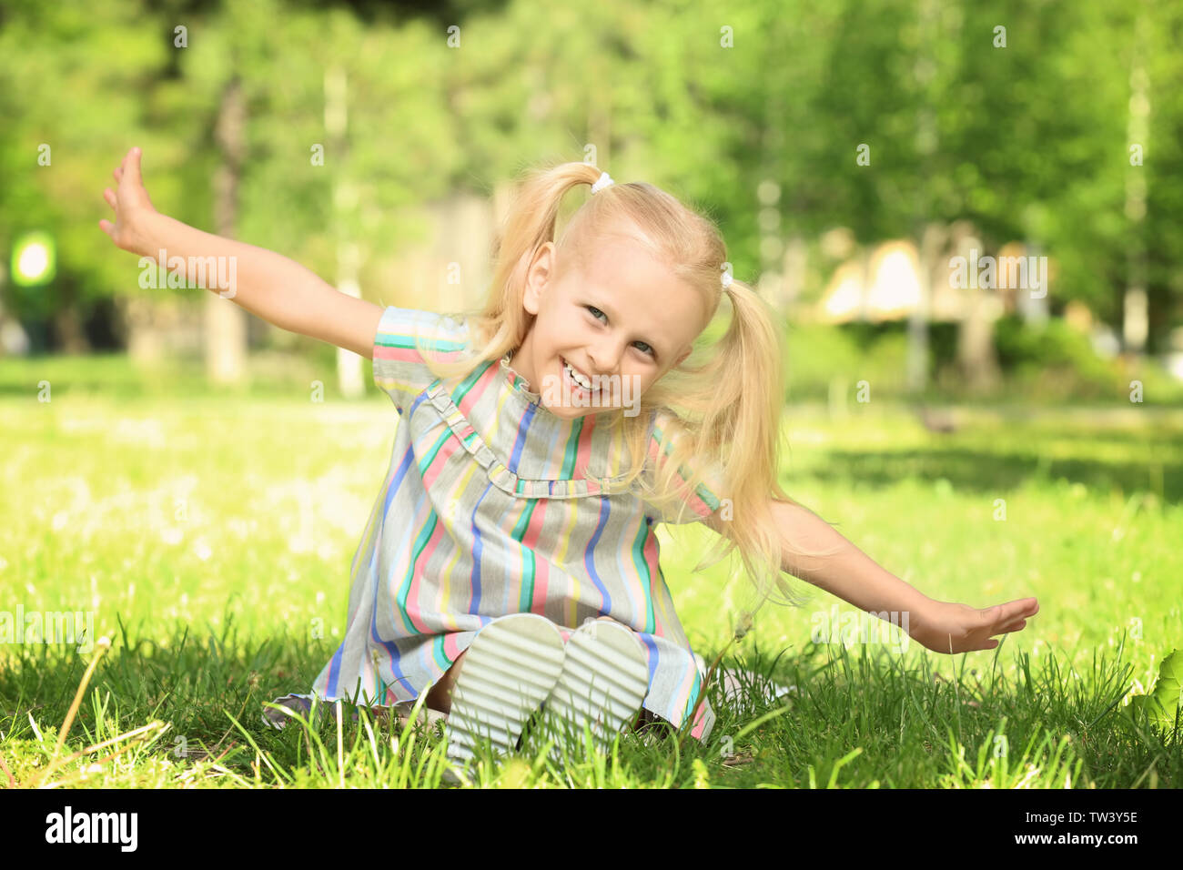 Cute little girl sitting on green grass in park Stock Photo - Alamy