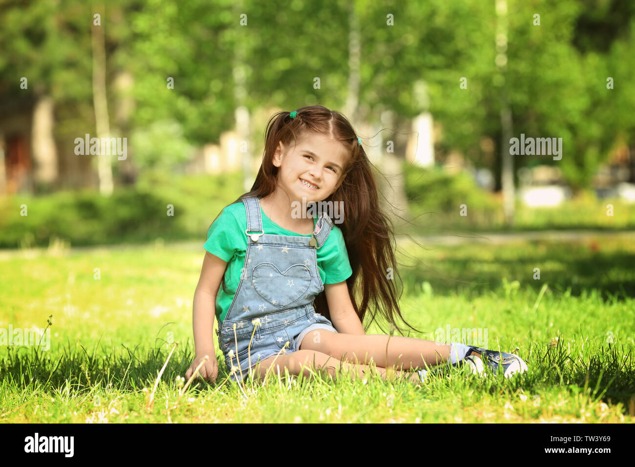 Cute little girl sitting on green grass in park Stock Photo - Alamy