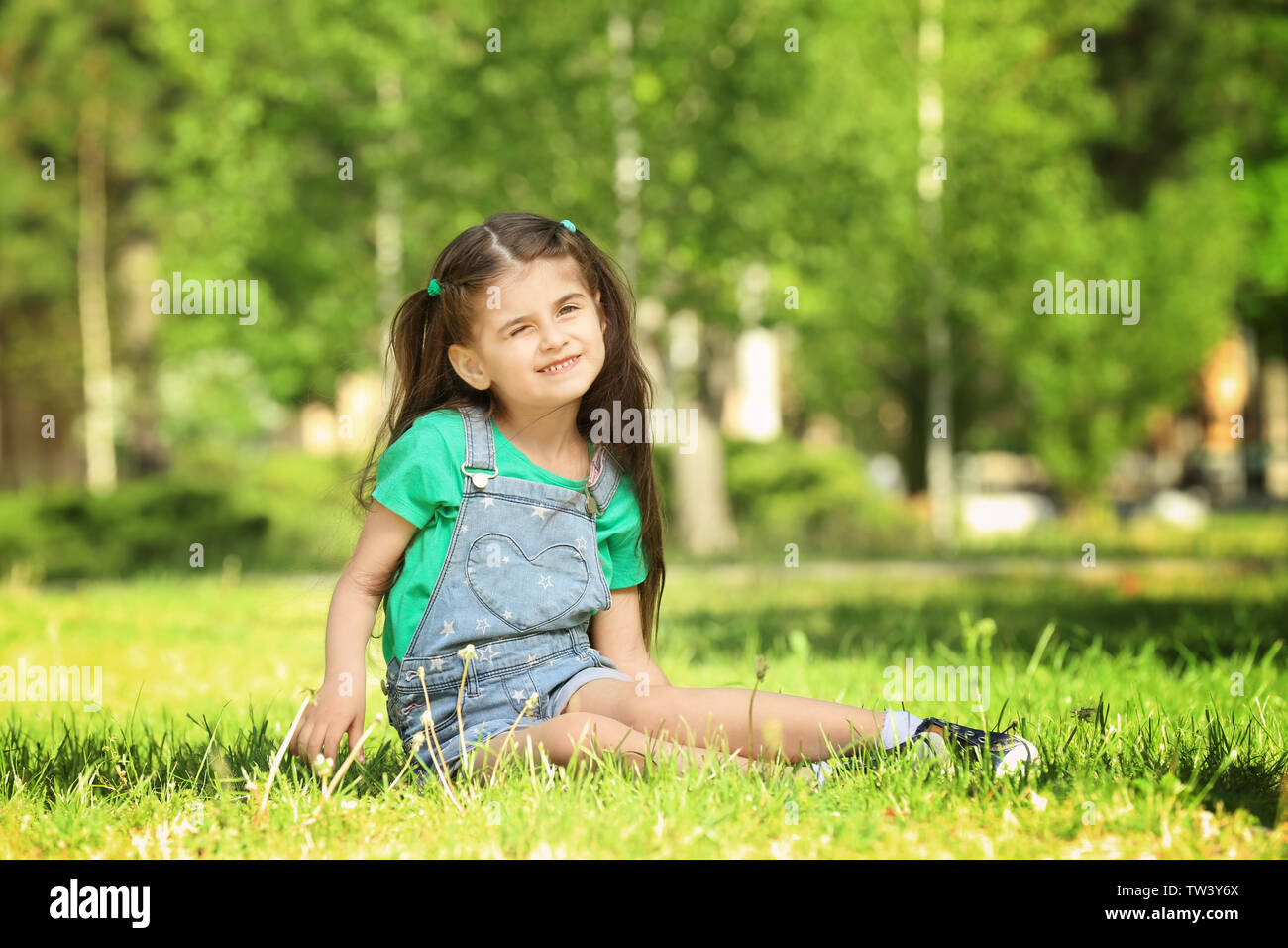 Cute little girl sitting on green grass in park Stock Photo - Alamy