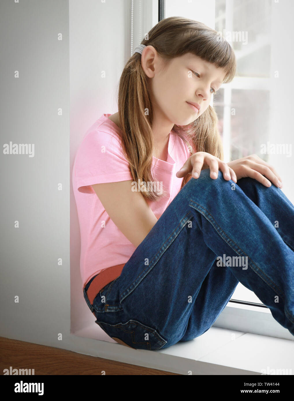 Sad little girl sitting on window sill at home Stock Photo - Alamy