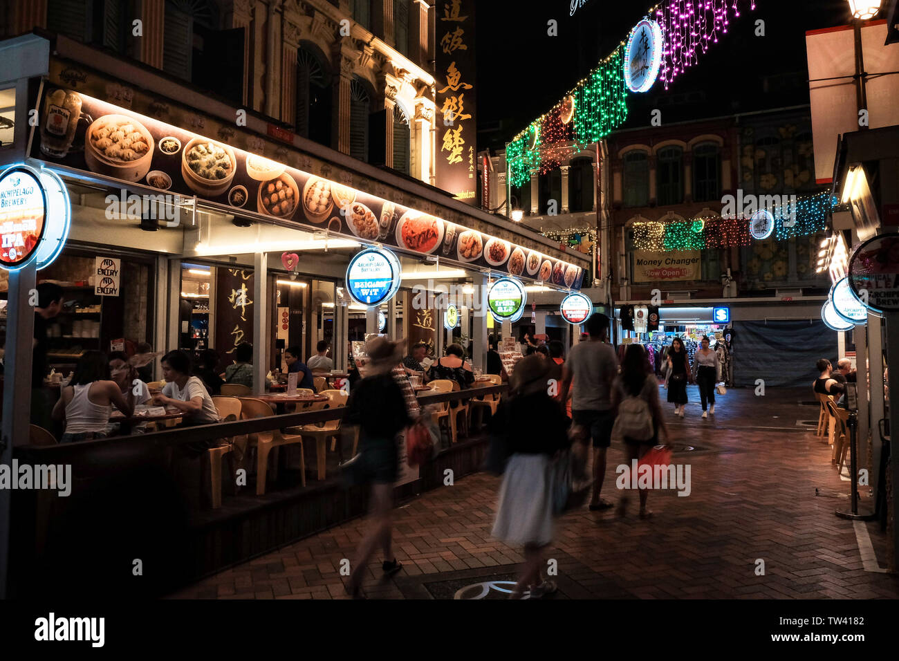 China town in Singapore at night showing restaurant and lights with passing pedestrians. Stock Photo