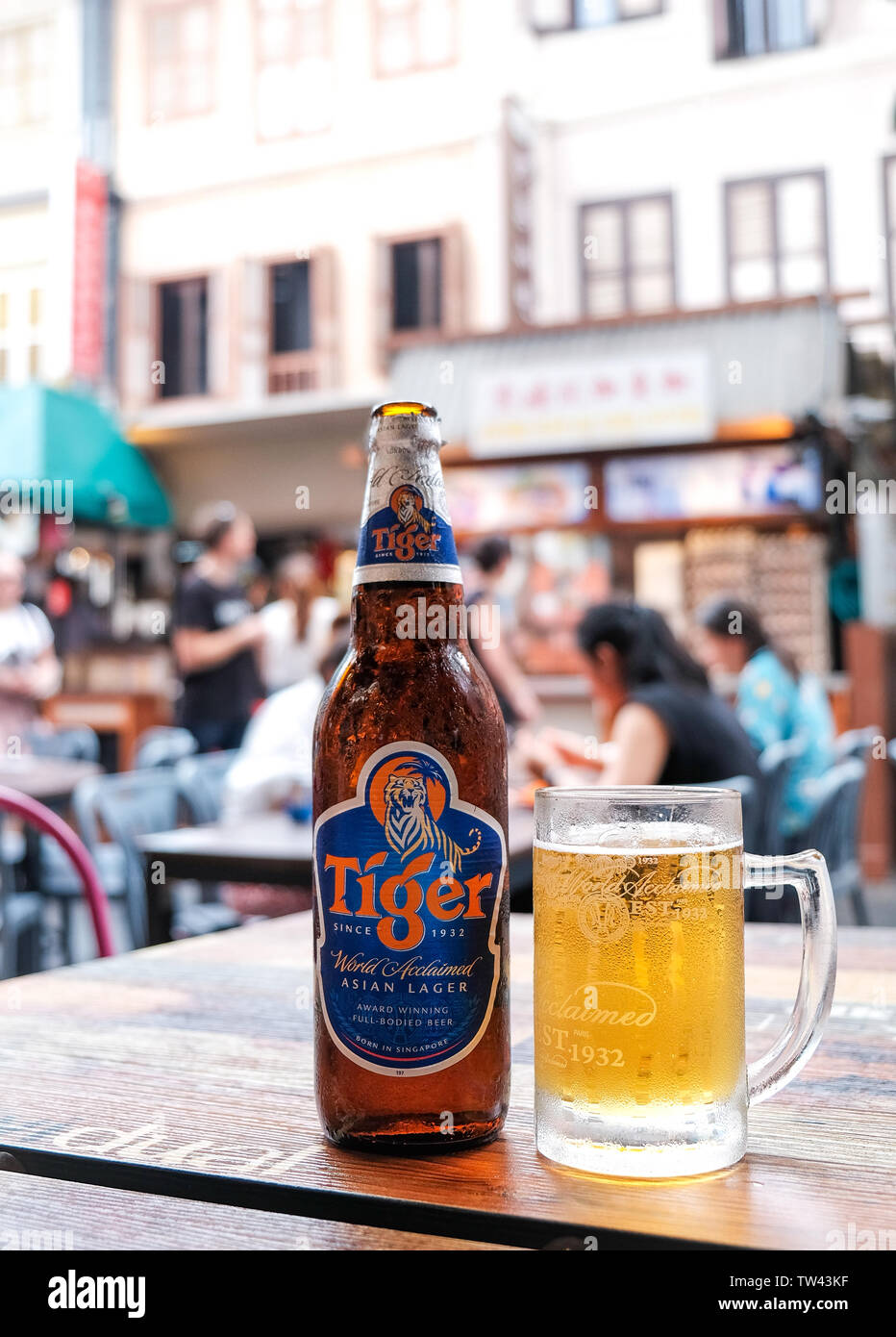 A bottle of Tiger beer with a full glass with Chinatown foodcourt  Singapore in the background. Stock Photo