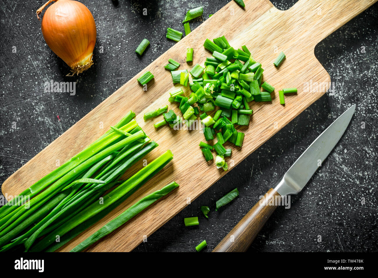 Chopped green onion on a cutting Board with a knife and onion. On dark ...