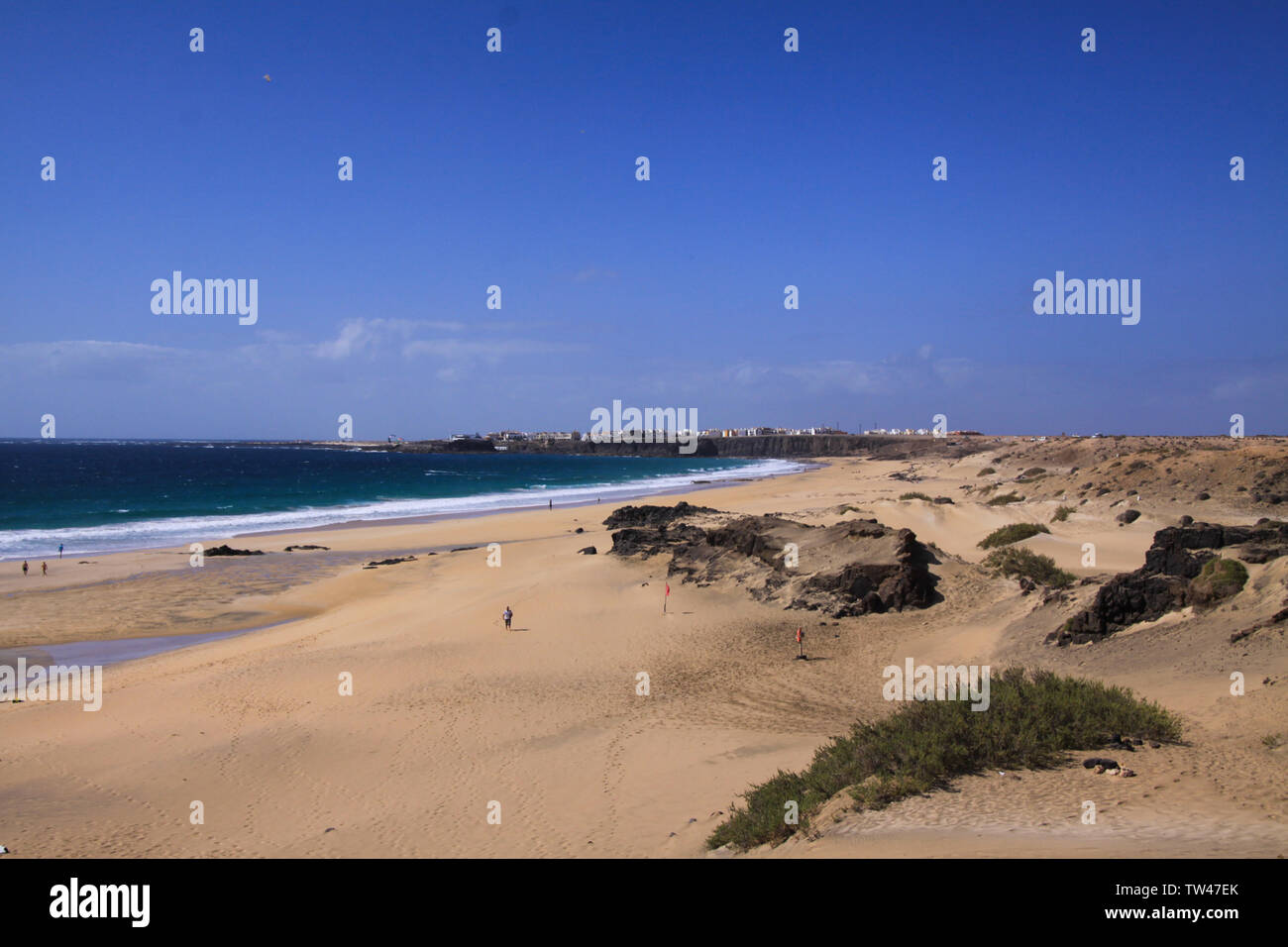 View over sand dunes with green ocean on (Playa del Aljibe) on white village on steep cliff (El Cotillo) - North Fuerteventura Stock Photo