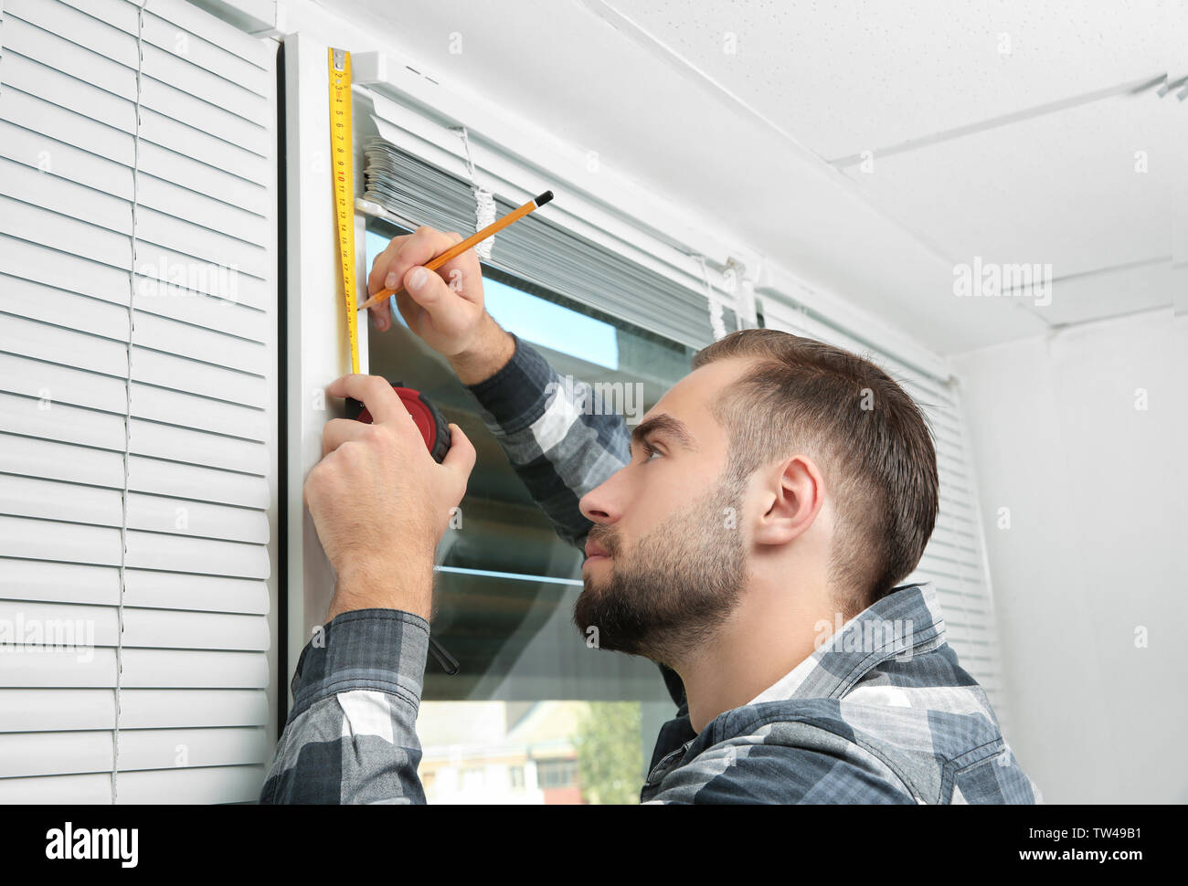 Young man installing window shades at home Stock Photo