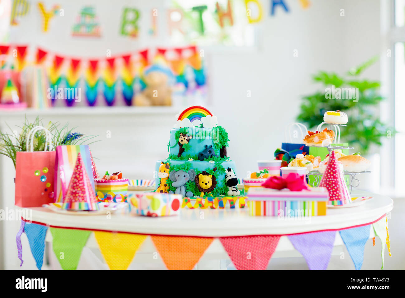 Cake for kids birthday celebration. Jungle animals theme children party. Decorated room for boy or girl kid birthday. Table setting with presents, gif Stock Photo