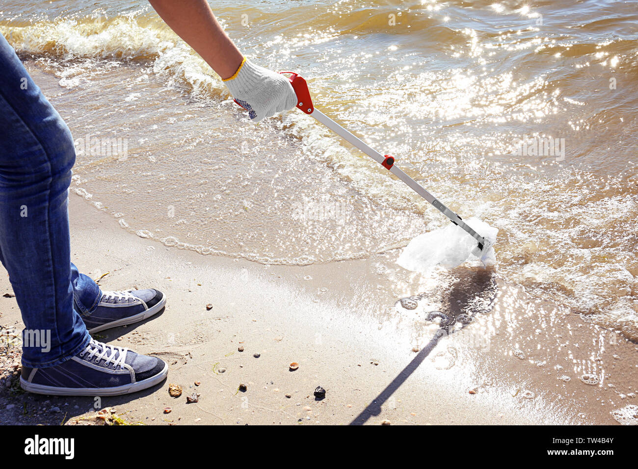 Young boy cleaning beach area with trash picker. Volunteer concept