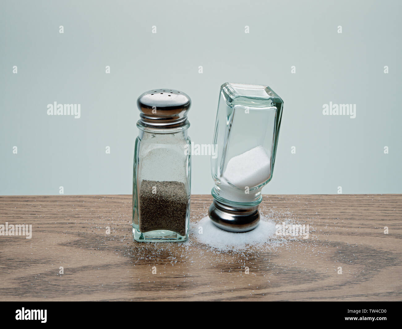 Balancing trick with upside down salt shaker balanced on spilled salt  beside tipped over pepper shaker on wood table Stock Photo - Alamy