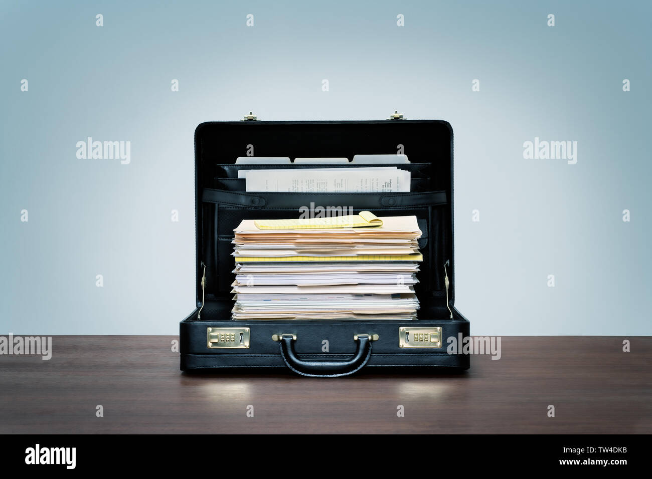 Tall stack of files and folders in black leather briefcase on wood desk