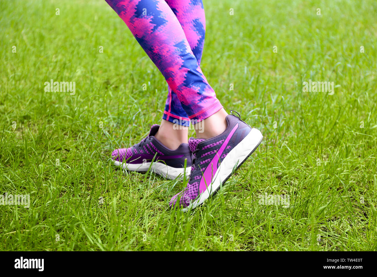 Female legs in leggings and purple sneakers on green grass Stock Photo