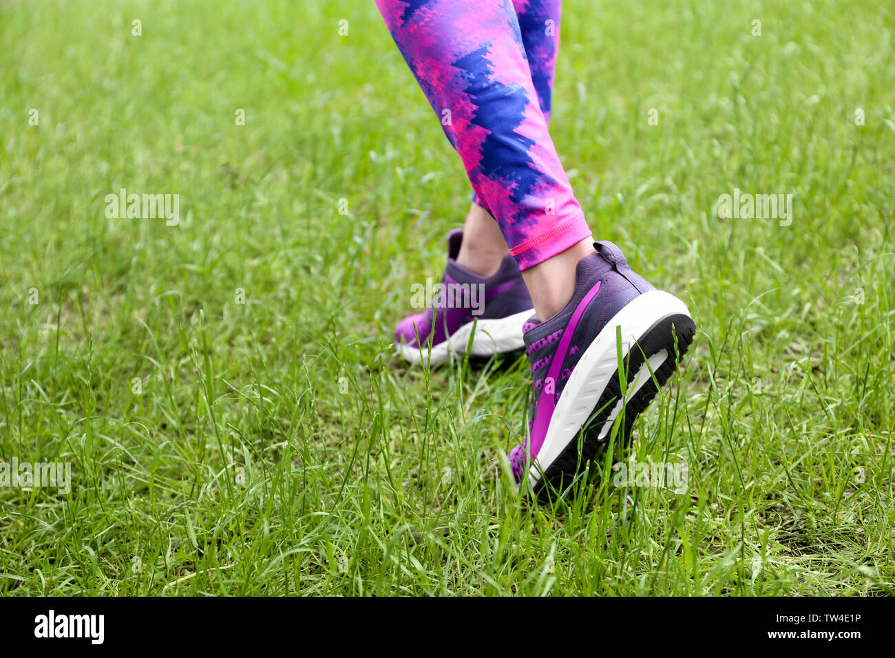Female legs in leggings and purple sneakers on green grass Stock Photo