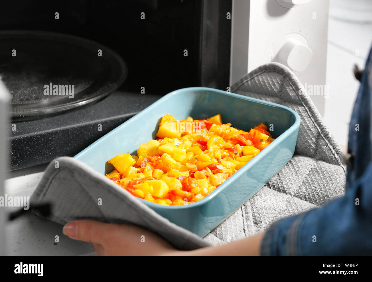 Woman taking out baking dish with dinner from microwave oven. Cooking
