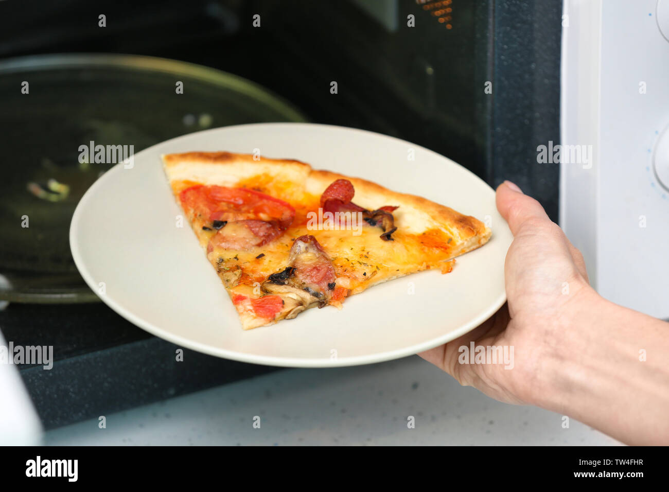 Woman putting plate with slice of pizza into microwave oven. Cooking for  one concept Stock Photo - Alamy