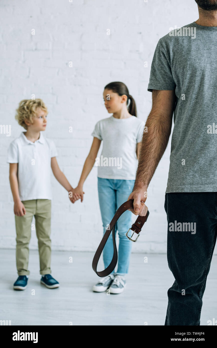 partial view of abusive father with belt and kids holding hands Stock Photo