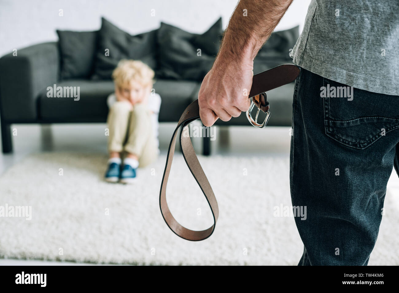 partial view of abusive father holding belt and sad son sitting on