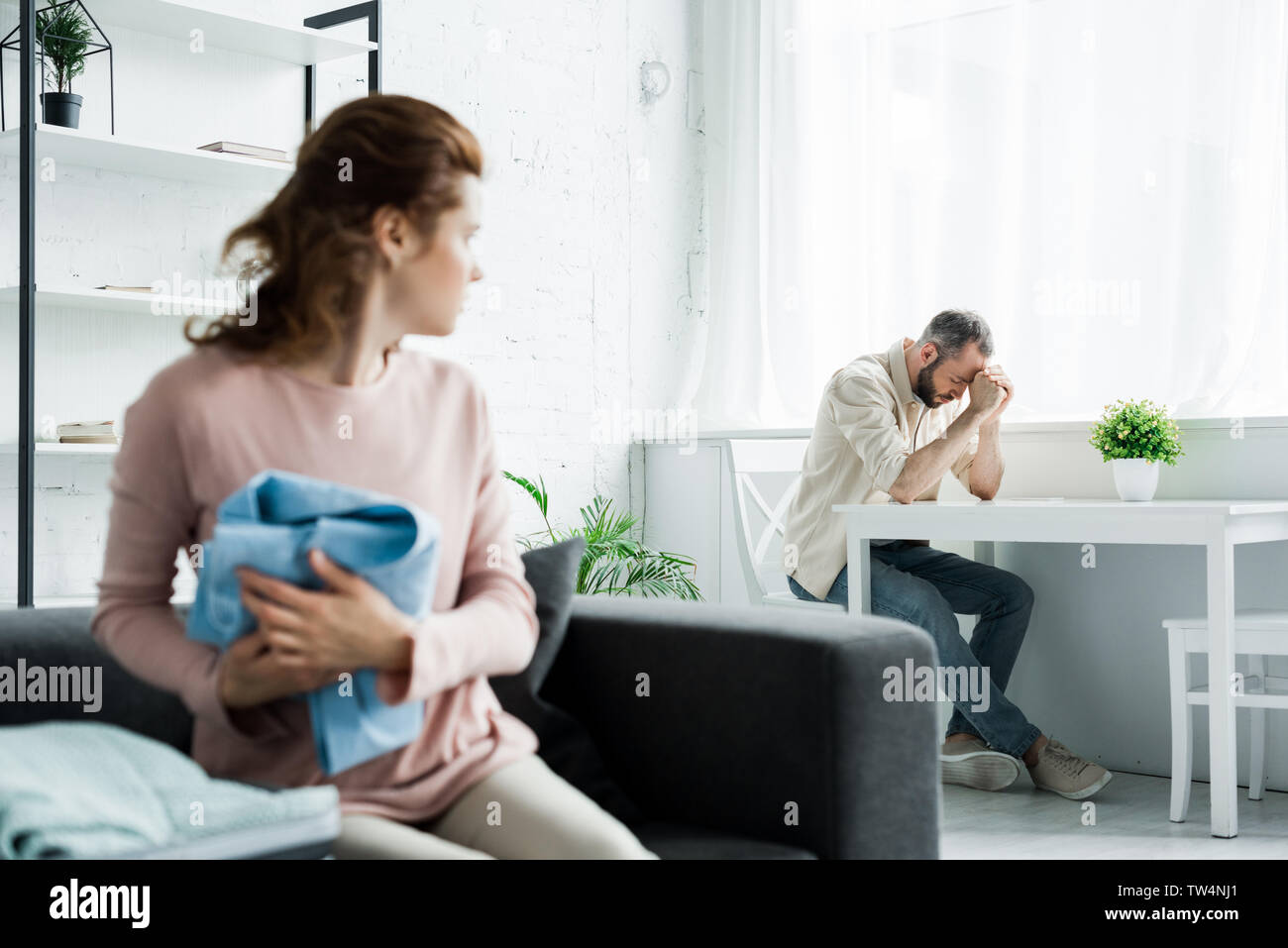 selective focus of frustrated man sitting on chair near table and upset woman with clothes in hands Stock Photo