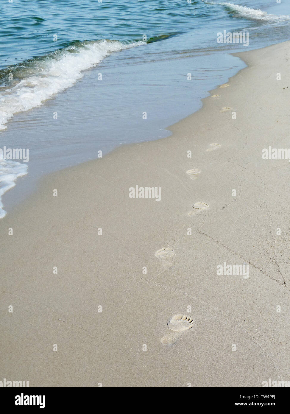 Footprints in sand at the beach vanishing in sea waves Stock Photo