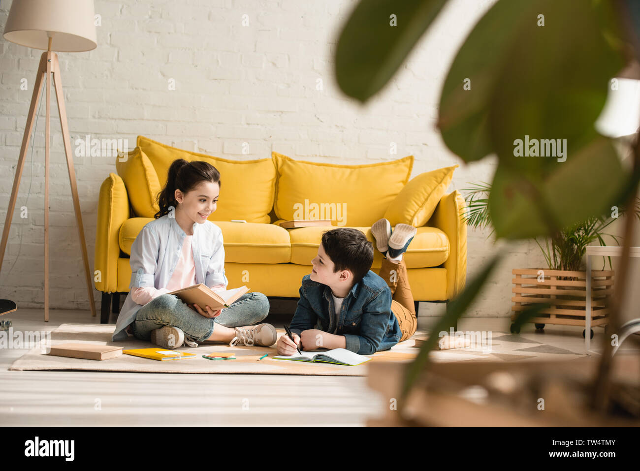 selective focus of cute boy lying on floor near sitting sister while doing schoolwork together at  home Stock Photo