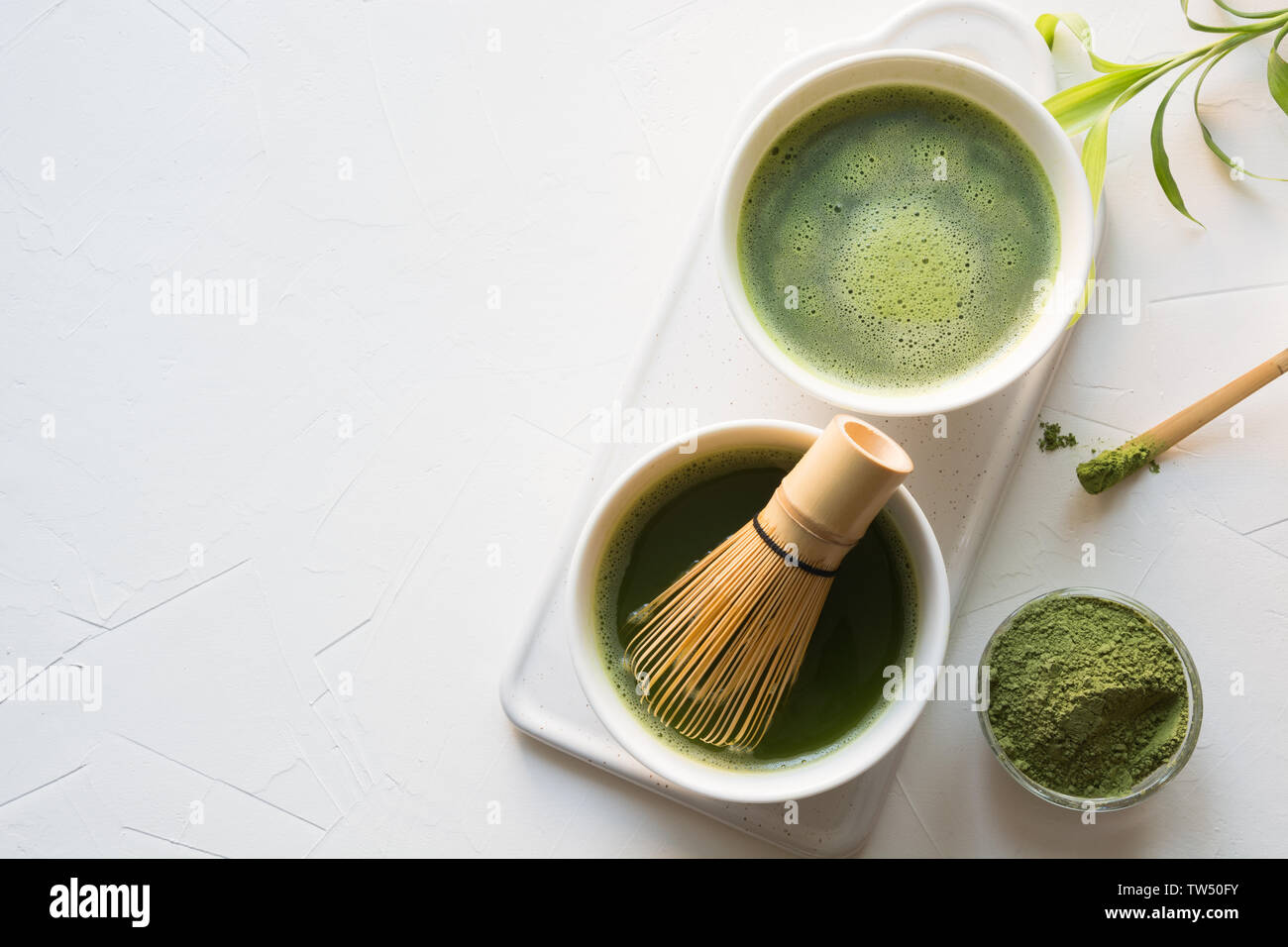 Ceremony traditional green matcha tea in bowl and bamboo whisk on white concrete table. Top view. Space for text. Stock Photo