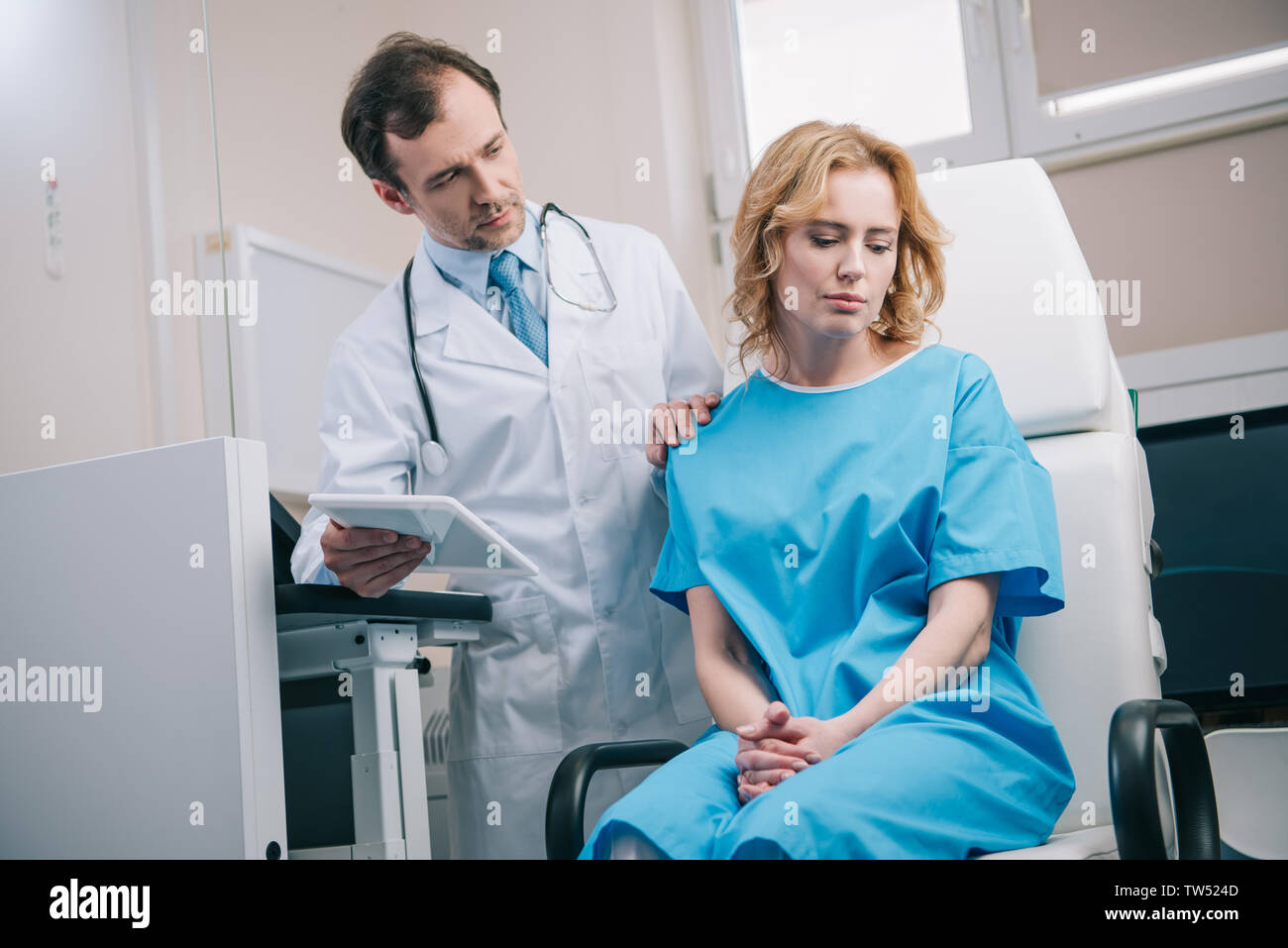 attentive doctor touching shoulder of upset woman while holding digital tablet Stock Photo