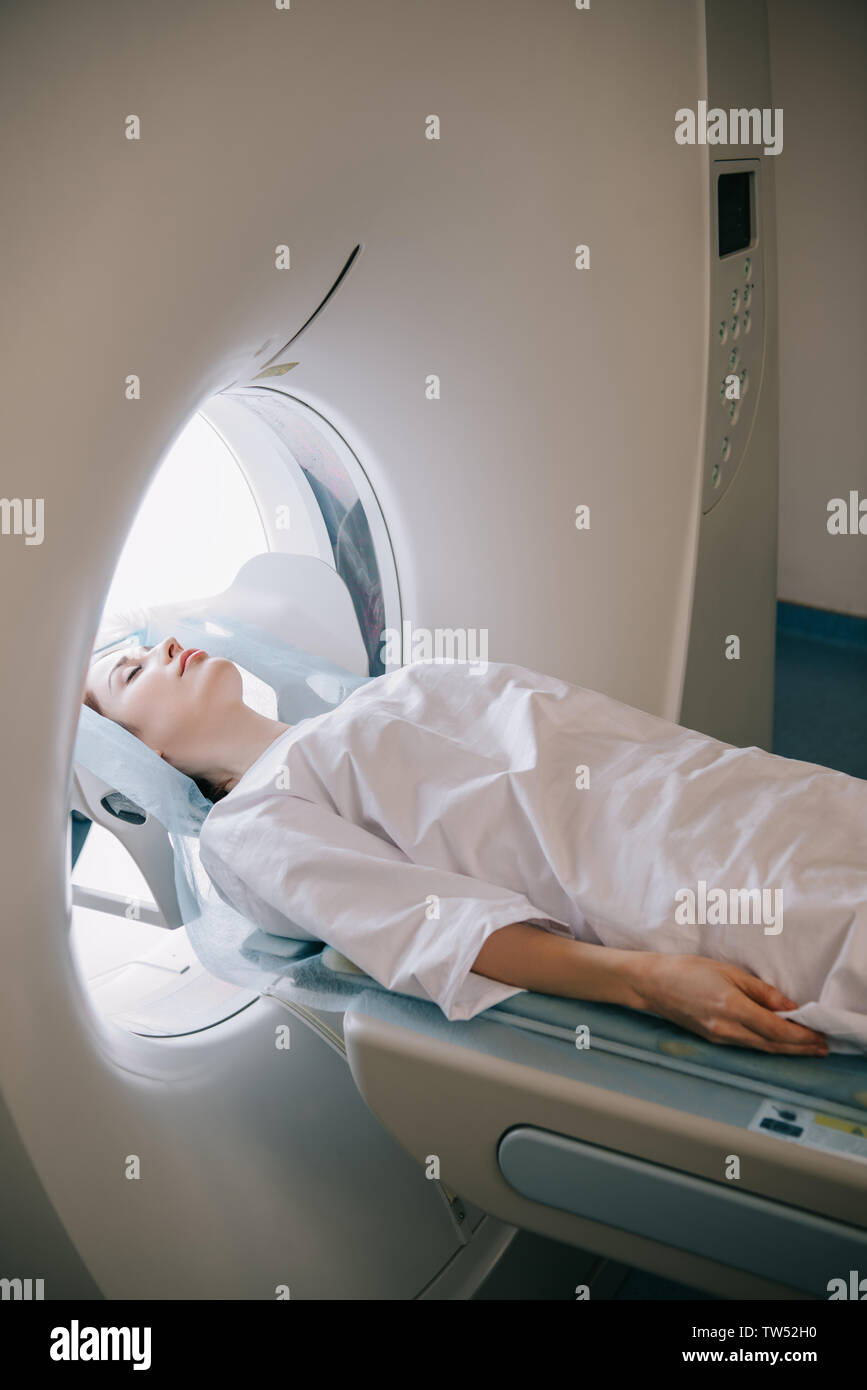 woman with closed eyes lying on computed tomography scanner table