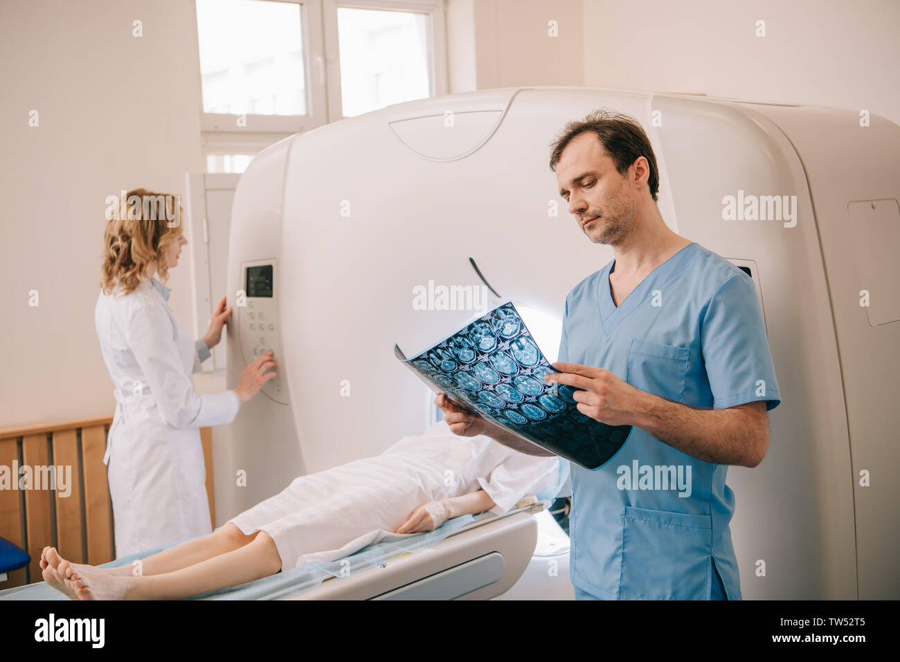 attentive doctor looking at tomography diagnosis while radiographer operating ct scanner during