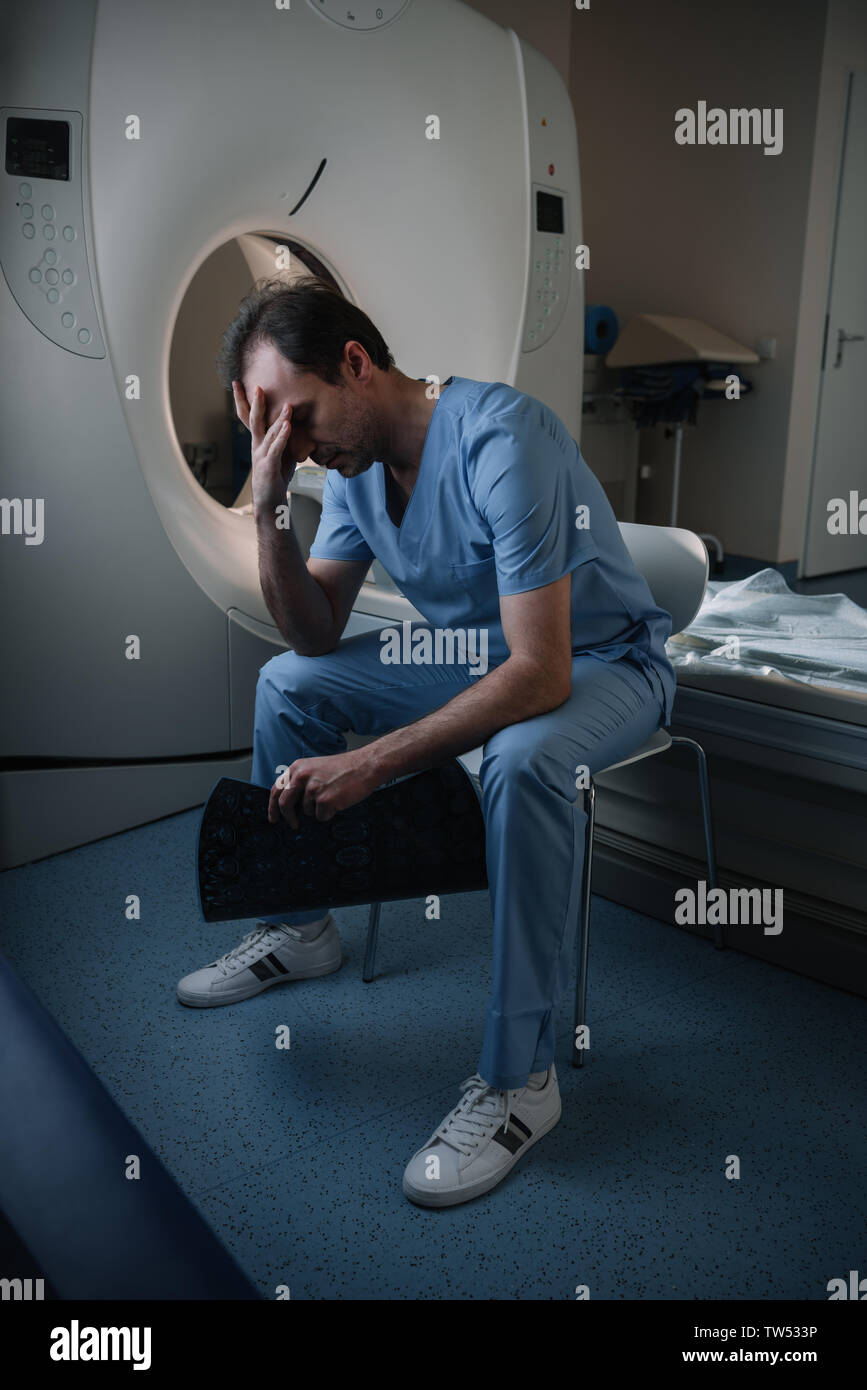 exhausted radiologist holding x-ray diagnosis while sitting near ct ...