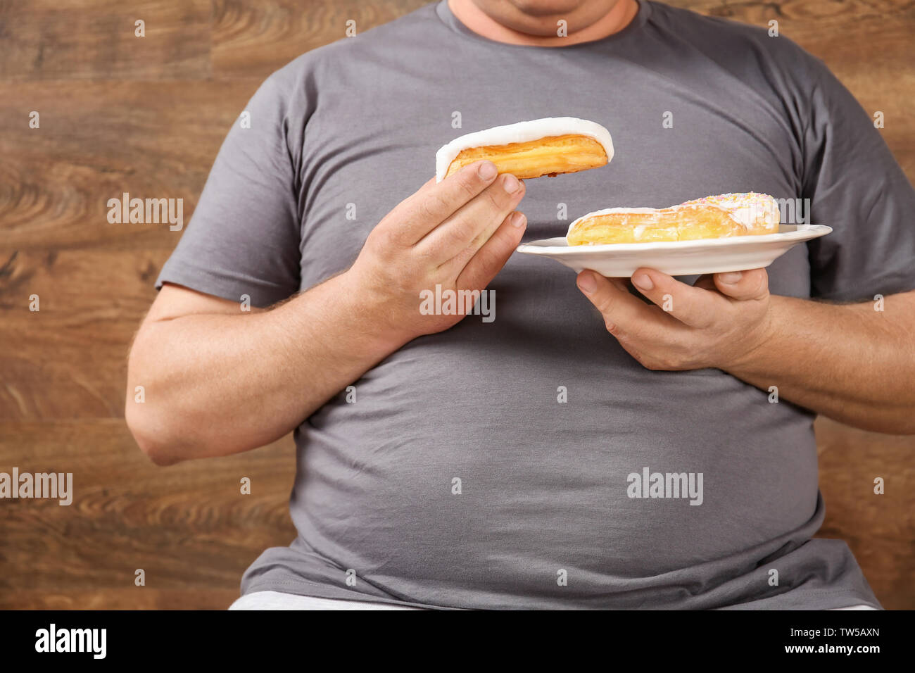 Overweight young man eating sweets on wooden background Stock Photo