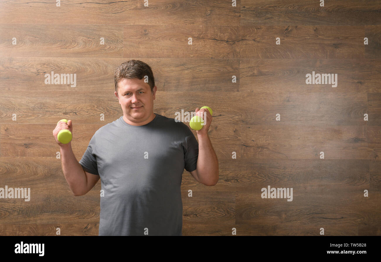 Overweight man with dumbbells on wooden background Stock Photo